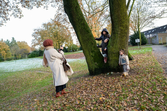 A family enjoys a playful moment in a park with autumn leaves on the ground during a sunny day, taking pictures, Netherlands