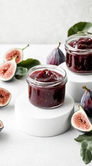 Homemade fig jam with caramel and reddish tones, presented in modern glass jars atop differently sized white podiums. Fresh figs and fig leaves create a natural, inviting arrangement. 