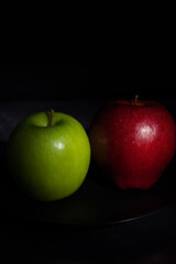Vertical image of fresh red and green apples on a black plate on a dark background. Fruit with sweet and sour taste