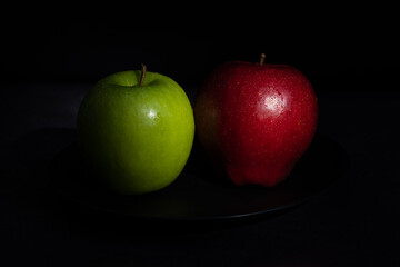 Fresh red and green apples on a black plate on a dark background. Fruit with sweet and sour taste