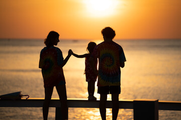 Family enjoys a sunset walk together on the beach wearing colorful tie-dye shirts
