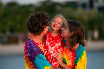 Family enjoys joyful moment on beach during sunset wearing colorful tie-dye shirts