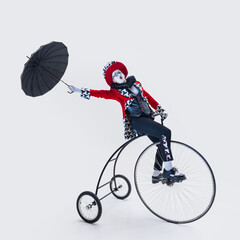 Elegant circus performer balancing on vintage bicycle while holding black umbrella in dramatic pose...
