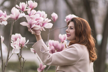 Fototapeta premium Woman magnolia flowers, surrounded by blossoming trees., hair down, wearing a light coat. Captured during spring, showcasing natural beauty and seasonal change.