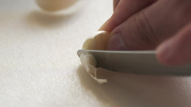 Chopping garlic with knife in close-up on white chopping board in slow motion