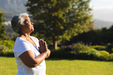 Senior woman meditating outdoors in peaceful garden, enjoying morning sunlight, copy space