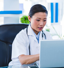 Doctor using laptop in office, focused on medical research and documentation