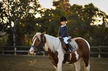 A young girl rider in a helmet and equestrian boots sits on her beloved horse at the stable, enjoying a peaceful horseback ride.