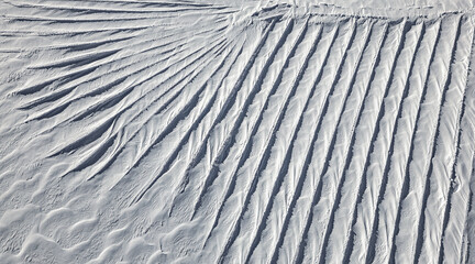 An aerial view of intricate snow formations on Glacier 3000 in the Swiss Alps. The wind has sculpted the snow into a mesmerizing pattern of parallel ridges and flowing textures. 