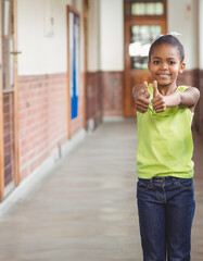 Smiling African American girl giving thumbs up in school hallway, copy space