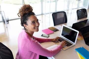 Smiling woman using laptop at office desk, working on project
