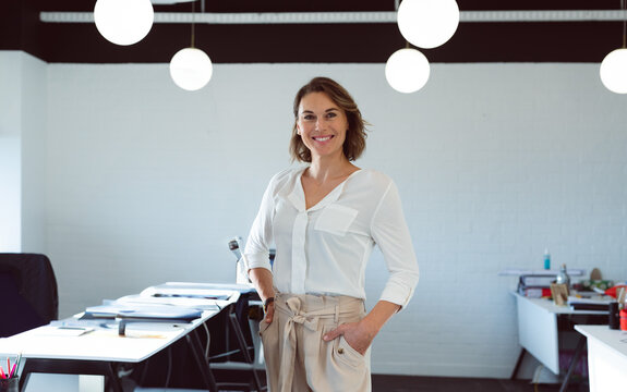 Confident businesswoman smiling in modern office, standing with hands in pockets