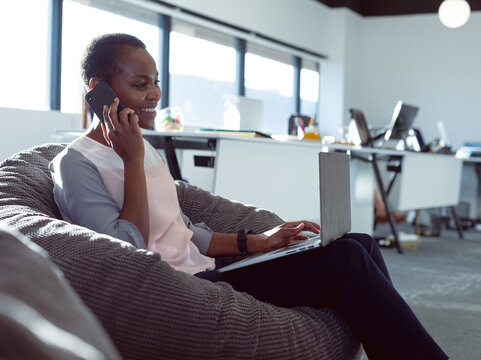 Smiling woman using laptop and talking on phone in modern office, copy space