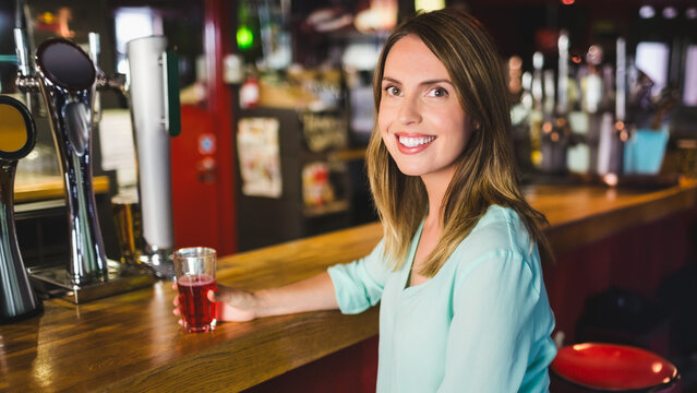 Smiling woman enjoying drink at bar counter in lively pub atmosphere