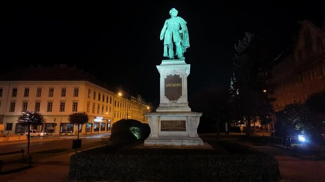 Beautifully illuminated statue of Szechenyi at night in a public square in Sopron, Hungary. The historical monument stands tall with surrounding lights.