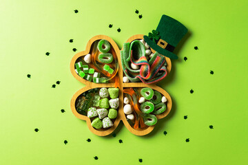 Shamrock tray filled with green candies and sweets, adorned with a small leprechaun hat on a light green background with scattered shamrock confetti. Perfect for St. Patrick's Day
