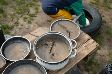 A lively mud kitchen in a kindergarten where children engage in free play, using pots, pans, and plates filled with sand, water, mud, and leaves. Montessori-inspired hands-on learning.