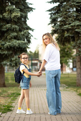 Fototapeta premium Woman mother and her charming little daughter. Mom leads little school child first day at school.