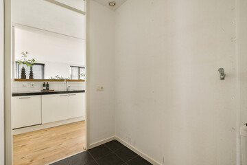 A clean, minimalistic interior showcasing a modern kitchen area with white cabinetry and wooden flooring, emphasizing simplicity and functionality.