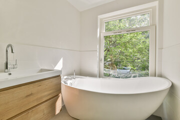 A sleek modern bathroom featuring a stylish freestanding bathtub, minimalist design elements, and large windows allowing natural light and a view of greenery outside.