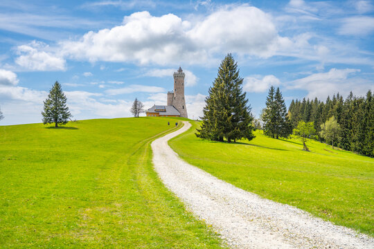 The Dalimil Lookout Tower stands prominently on Vetrov Hill, showcasing its replica design. It's a serene landscape with lush grass and tall trees, offering a picturesque view of the surroundings.