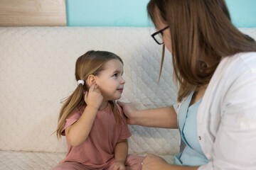 Female pediatrician examines ear of sick child during home visit. Doctor carefully conducts medical examination of sick child in familiar environment. Concept medicine and health care.