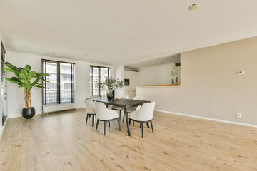 A stylish, modern dining area featuring a wooden table, elegant chairs, and a large potted plant, illuminated by natural light streaming through windows.