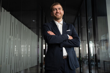 Confident businessman, entrepreneur, or executive in a navy blue suit standing in a modern office...