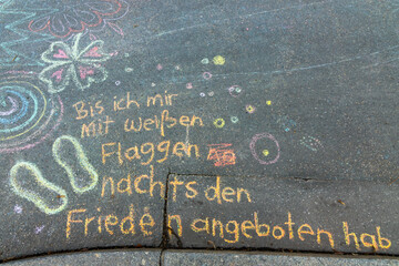 Words in German mean Until I will wave my white flag. Vibrant crayon drawings cover the asphalt, showcasing playful shapes, doodles, and creative expressions. A joyful scene of children's outdoor crea