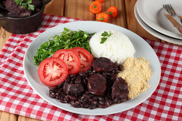 Comida tipica brasileira:  feijoada com acompanhamentos, servida no prato e na tigela