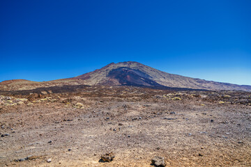 Barren, rocky landscape with a large volcanic mountain in the background, featuring various shades...