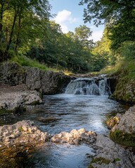Obraz premium Tranquil Waterfall Cascading Through Lush Green Forest Rocks and Trees under Bright Blue Sky in Natural Sunlight Serene Landscape