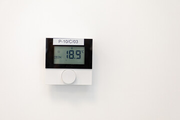 A modern thermostat mounted on a sleek white wall clearly displays its various temperature settings