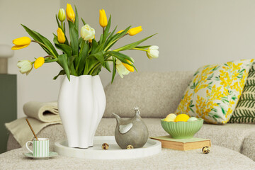 Easter-inspired home decor with yellow tulips, a whimsical ceramic chicken, and pastel-colored eggs in a vintage-style green bowl. A neutral background enhances the vibrant seasonal details.