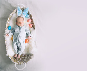 Cute baby Easter bunny. Little baby boy with bunny ears and Easter eggs in wicker basket in white...