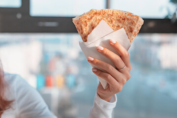 Woman's hand holding a folded crepe in white paper wrap in front of a blurred office window