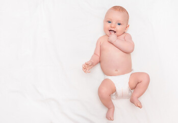 cute baby in diaper lying on back, smiling and holding hand in mouth