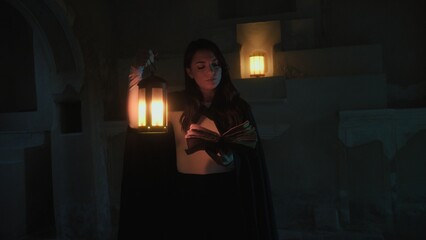 Woman Reads Mysteries On Magic Book In Ancient Cave At Night With Lantern