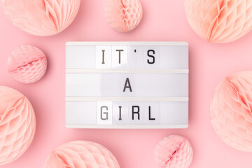 It's a girl. Lightbox with letters and tissue paper balls in a pink color. Baby shower composition.