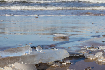 
chunks of ice on a sandy beach with water and waves in the background.