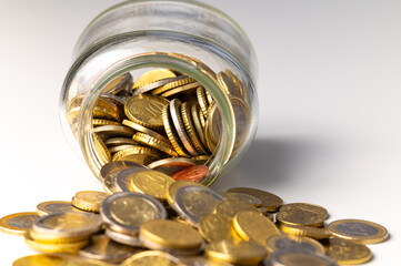 Glass jar turned upside down, with coins spilling out. Piggy bank and savings.