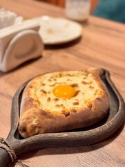 Georgian dish Adjarski Khachapuri on a dark wood serving board on a wooden table