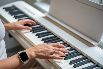 Fototapeta premium Closeup woman's hand playing piano. Concept of home lesson of music: learning music enhances motor skills, hearing, and intelligence, fostering creativity