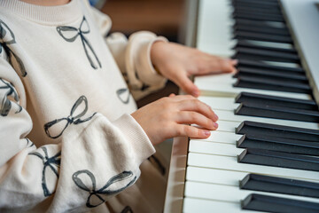 Fototapeta premium Close up view of small hands of girl on white piano synthesizer. Concept of early development: learning music enhances motor skills, hearing, and intelligence, fostering creativity from childhood