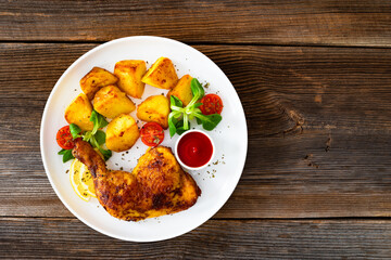 Oven roasted chicken thigh with fried potatoes and fresh salad on wooden table	