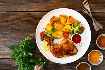 Oven roasted chicken thigh with fried potatoes and fresh salad on wooden table	