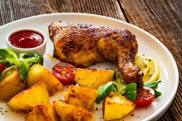 Oven roasted chicken thigh with fried potatoes and fresh salad on wooden table	