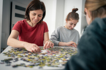Fototapeta premium Mother And Daughters Assembling Puzzles On A Table As The Family Spends Time Together