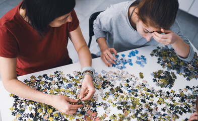Mother And Daughters Assembling Puzzles On A Table As A Weekend Family Hobby