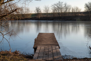 Winter river bank with wooden pier and bare trees